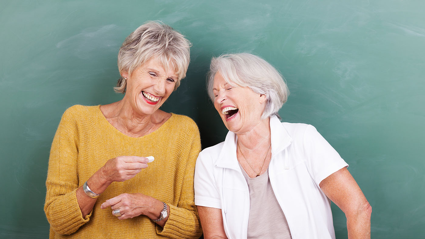 Zwei Frauen stehen lachend vor einer Tafel.